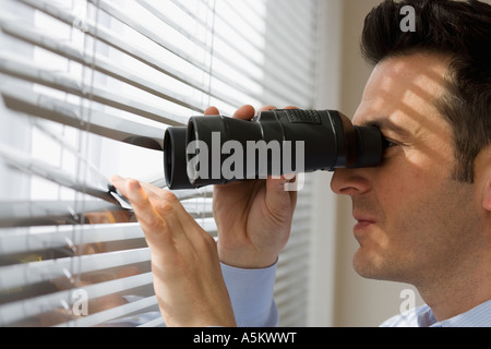 Businessman looking out window through binoculars Stock Photo