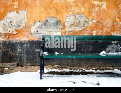 Green bench in snow against decaying stucco wall Stock Photo