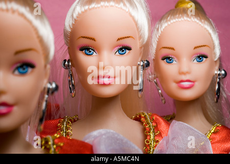three identical female dolls with blond hair blue eyes head and shoulders pink background narrow focus on middle Stock Photo