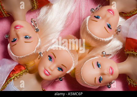 Birdseye view of four identical female dolls with blond hair blue eyes head and shoulders pink background Stock Photo