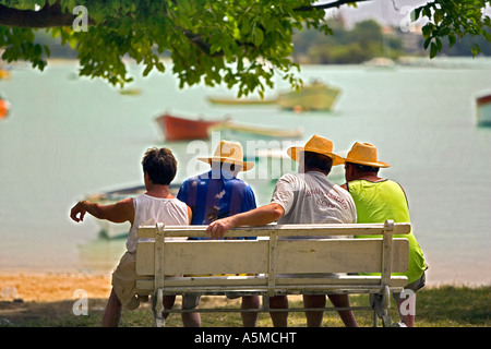 Hot day in Mauritius -  Four men relaxing in the heat watching the fishing boats in the bay Stock Photo