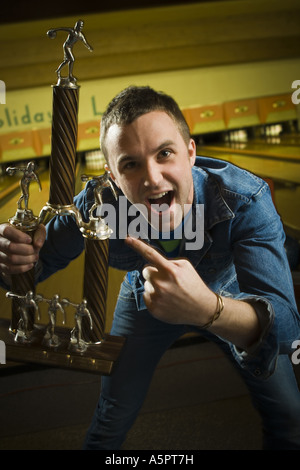 Portrait of a young man holding a bowling trophy and laughing Stock Photo