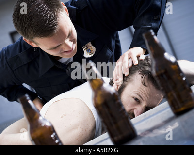 Police officer arresting man lying down with beer bottles Stock Photo