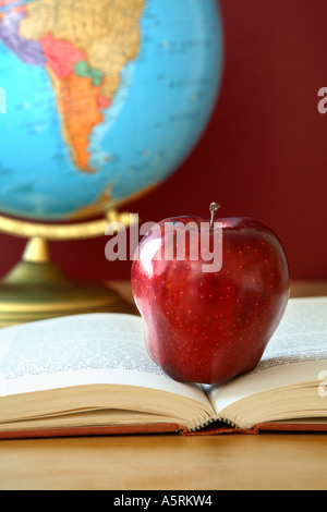 School still life with red apple on open book with globe in background. Stock Photo
