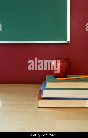 Classroom desk with books, apple pencil and chalkboard in background Stock Photo