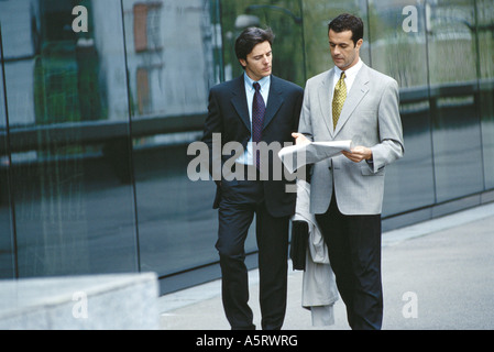 Two businessmen walking, one gesturing toward newspaper Stock Photo