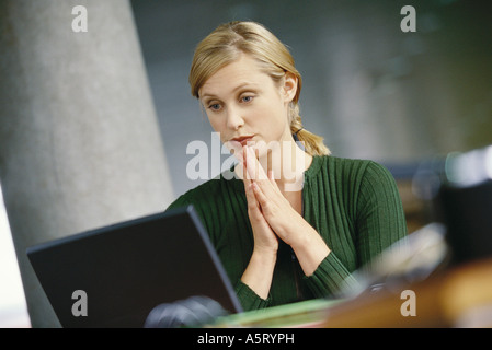 Young woman using laptop, hands clasped in front of chin Stock Photo