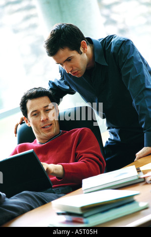 Man using laptop, talking to second man looking over shoulder Stock Photo