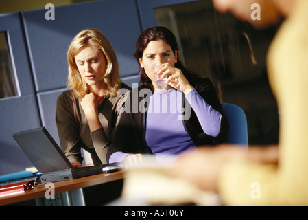 Two female office workers using laptop, one drinking glass of water Stock Photo