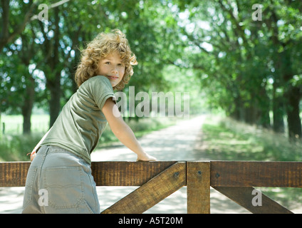 Boy leaning against wooden fence, looking over shoulder at camera Stock Photo