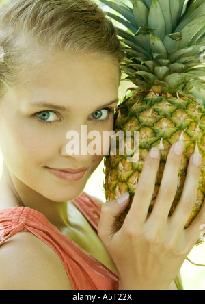 Woman holding pineapple next to face, smiling at camera Stock Photo