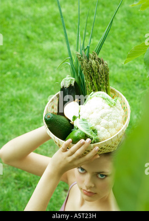 Woman holding basket full of fresh vegetables on top of head Stock Photo