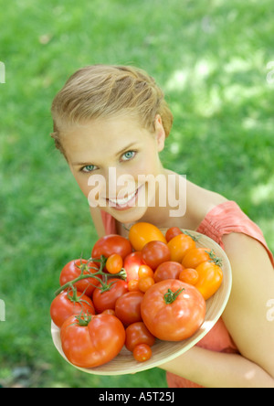 Young woman holding up bowl of tomatoes, smiling at camera Stock Photo