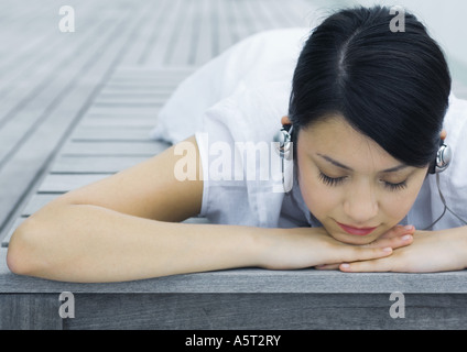 Woman lying on deck, listening to headphones Stock Photo