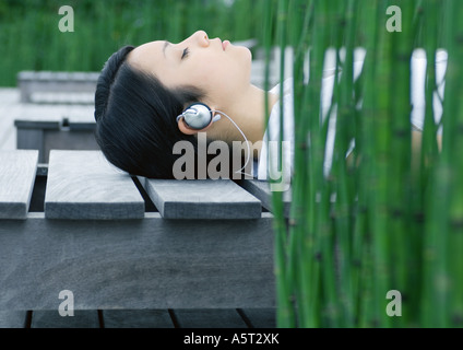 Woman lying on wooden lounge chair, listening to headphones Stock Photo