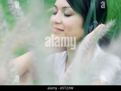 Woman listening to headphones, vegetation in foreground Stock Photo