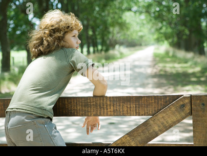 Boy hanging on fence, dirt road in background Stock Photo