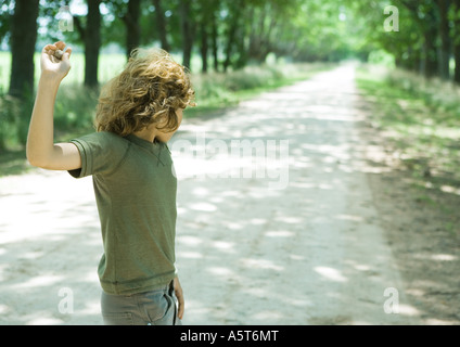 Boy standing in middle of dirt road, throwing pebbles Stock Photo