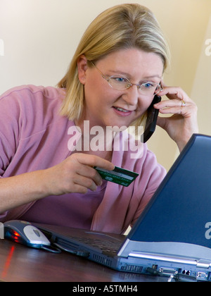 Woman shopping on line using her laptop computer flip mobile telephone and credit card Stock Photo