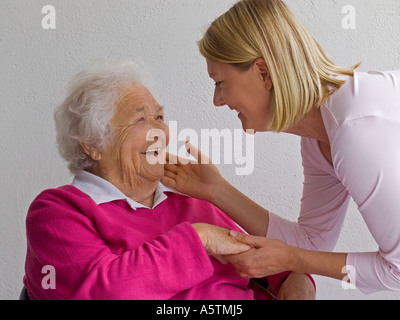 ELDERLY & Young caring carer visitor woman affectionately tactile  greeting happy smiling elderly senior old aged retired lady in natural light Stock Photo