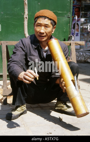 local man in traditional blue jacket smoking a cigarette through a large bamboo pipe on the street kunming yunnan province china Stock Photo