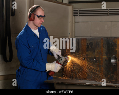 Man wearing protective gloves goggles and ear protectors using angle grinder on iron block sparks heat friction Stock Photo