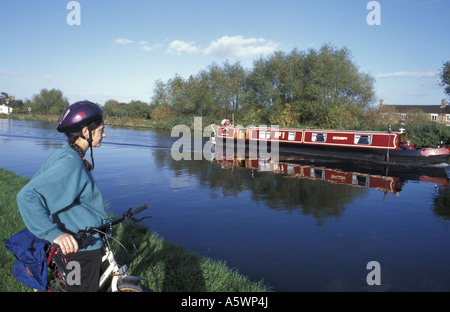 A cyclist watches as narrowboat passes near Frampton Upon Severn on the Gloucester sharpness Canal in Gloucestershire England Stock Photo