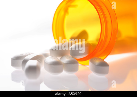 Prescription bottle with pills spilling out on reflective surface. Stock Photo