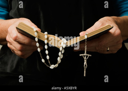 A woman's hand holding rosary beads and a prayer book while praying Stock Photo