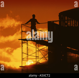 silhouette of construction worker wearing hard hat on scaffolding yellow orange sky Stock Photo