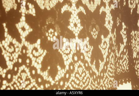 Shadow on a white wall in warm light of the lower part of an intricately patterned net curtain or tablecloth Stock Photo