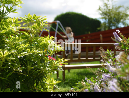 Child playing on garden swing viewed through flower bed Stock Photo
