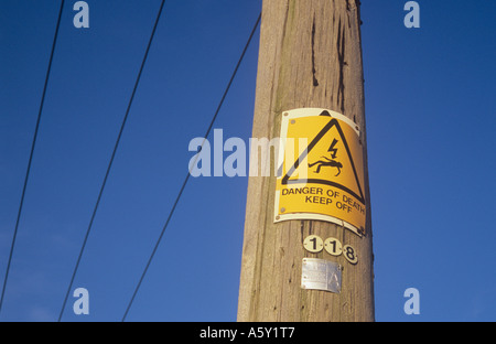 Yellow sign with iconic man being electrocuted and words Danger of death Keep off nailed over older sign on electricity pole Stock Photo