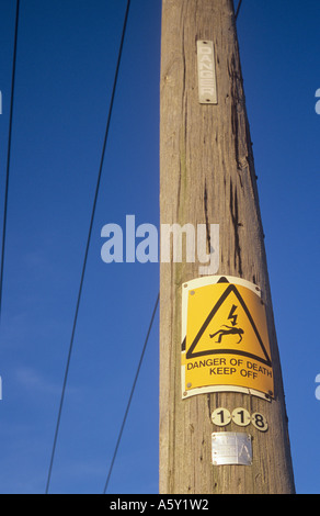 Yellow sign with iconic man being electrocuted and words Danger of death Keep off nailed over older sign on electricity pole Stock Photo