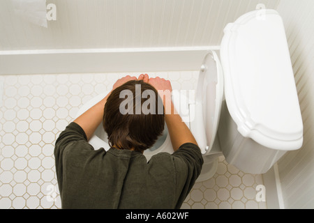 overhead view of male teenager bent over toilet being sick Stock Photo