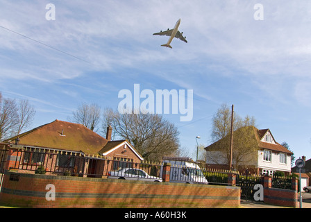 Horizontal view of aircraft taking off from Heathrow airport, flying low over residential homes against a blue sky. Stock Photo