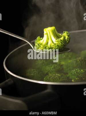 SPOON HOLDING FLORETTE OF BROCOLLI OVER PAN OF BOILING WATER FULL OF BROCOLLI WITH RISING STEAM SIMMERING ON GAS COOKER Stock Photo