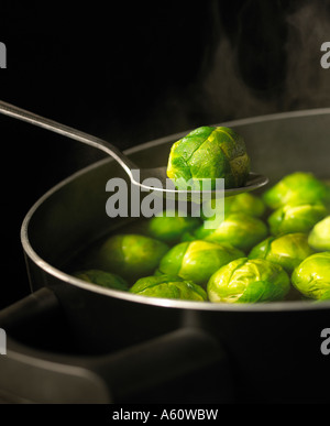 SPOON HOLDING BRUSSELS SPROUT OVER PAN OF BOILING WATER FULL OF SPROUTS WITH RISING STEAM SIMMERING ON GAS COOKER Stock Photo