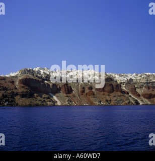 Clifftop view of Oia in early morning sunshine spread out along top edge of red volcanic rocks on Santorini Greek Islands Stock Photo