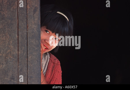 Shy local girl peeks from behind the doorframe Shwe Mine Bone village Shan State near Kalaw Burma Stock Photo