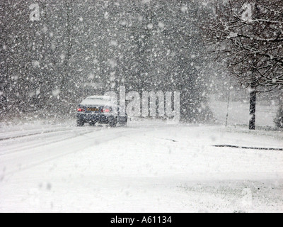 Falling snow back rear view of car driving in icy conditions covering rural road in blizzard weather winter scene near Brentwood Essex England UK Stock Photo