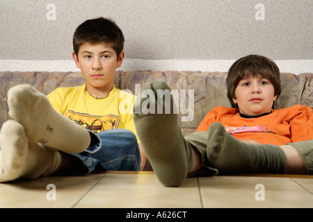 portrait of two young boys glued to the television with their feet on the table Stock Photo