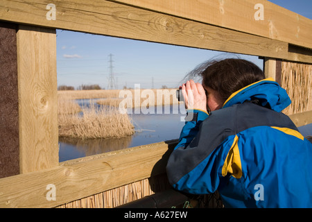 Woman using binoculars in hide at Newport Wetlands National Nature Reserve Newport Wales UK Stock Photo