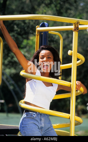 Black african american woman in her 20s outdoors on yellow bars playground set having fun and laughing Stock Photo