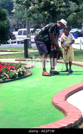 Balck African American man playing minature golf with young children Stock Photo