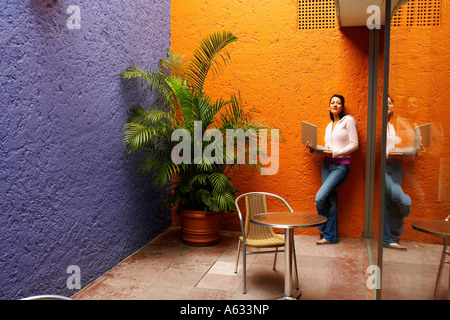 Portrait of a mid adult woman leaning against a wall and holding a laptop Stock Photo