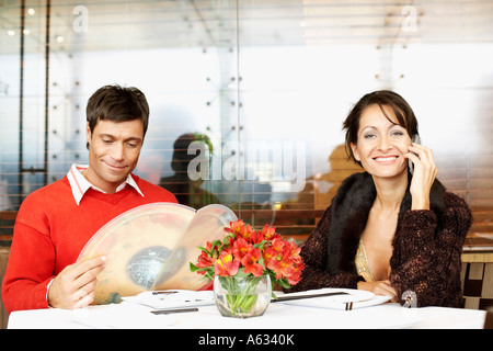 Mid adult woman talking on a mobile phone with a mid adult man looking at menu in a restaurant Stock Photo