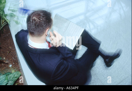 High angle view of businessman talking on mobile phone while reading financial newspaper Stock Photo