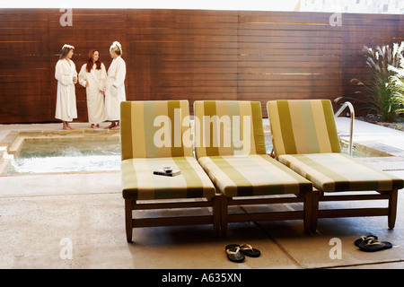 Three empty lounge chairs with three women in the background Stock Photo