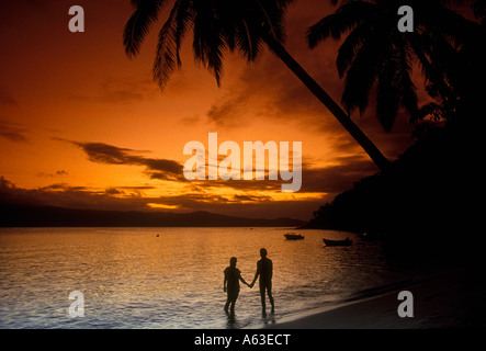 People adult man and woman romance romantic couple lovers holding hands on beach at sunset Qamea Island Fiji Melanesia Oceania Stock Photo